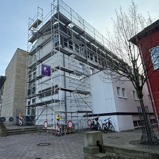 Ein mehrstöckiges Gebäude ist von einem silbernen Gerüst umgeben, was auf Bauarbeiten hindeutet.